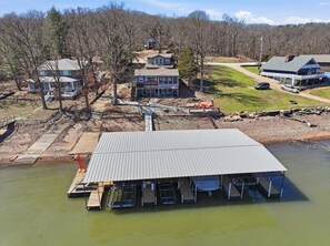 A waterfront property with a covered dock, a building with a porch, and a small boat dock. - Zero-step Dock Life With Big Views, Lake Toys, Firepit, Boat Slip at 43mm (Roach)