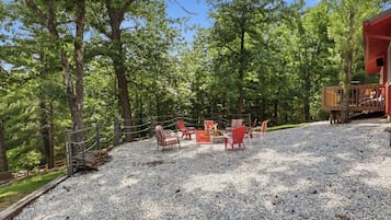 A gravel patio with outdoor seating and a fire pit, surrounded by trees.