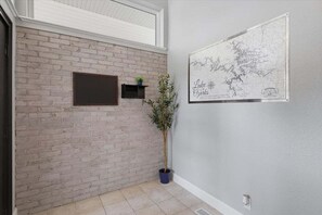 Una habitación con pared de ladrillo, un mapa colgado, una planta en maceta y un estante pequeño con una planta.