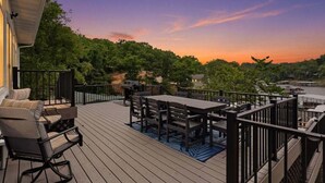 Eine Holzterrasse mit Gartenmöbeln, Blick auf Bäume und einem Sonnenuntergang.
