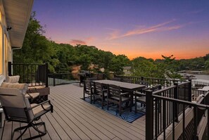 Eine Holzterrasse mit Gartenmöbeln, Blick auf Bäume und einem Sonnenuntergang.