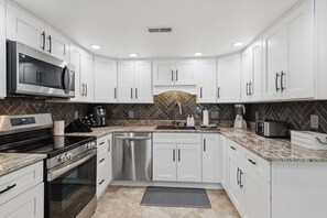 A modern kitchen with white cabinets, stainless steel appliances, a herringbone tile backsplash, and a granite countertop. - Lakefront Cove Retreat With Private Dock, Slide & Room to Gather (Rocky Mount)
