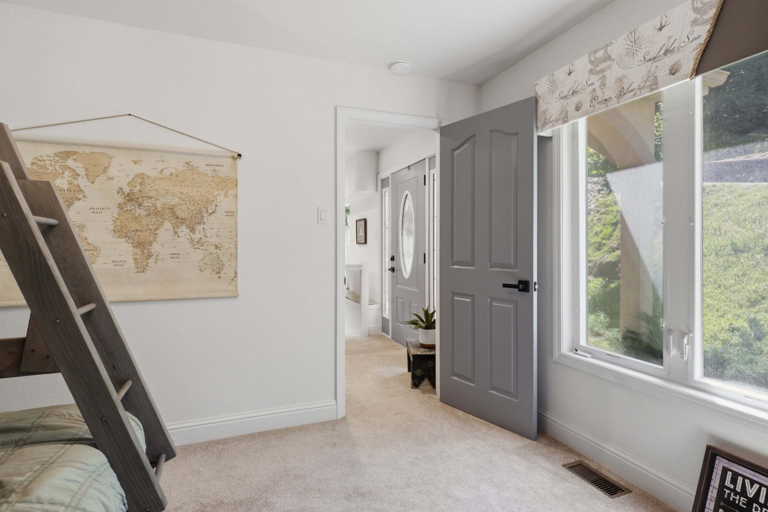 A hallway with a world map, a door, and a window with a view of greenery.