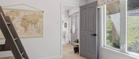 A hallway with a world map, a door, and a window with a view of greenery.