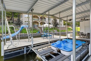 A covered boat dock with a water slide, a pool table, and a building in the background.