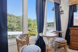 A room with a view of a lake, a table, two chairs, and a wooden cabinet.