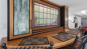 Un comedor con una gran mesa de madera, sillas negras y un ventanal de vitral.