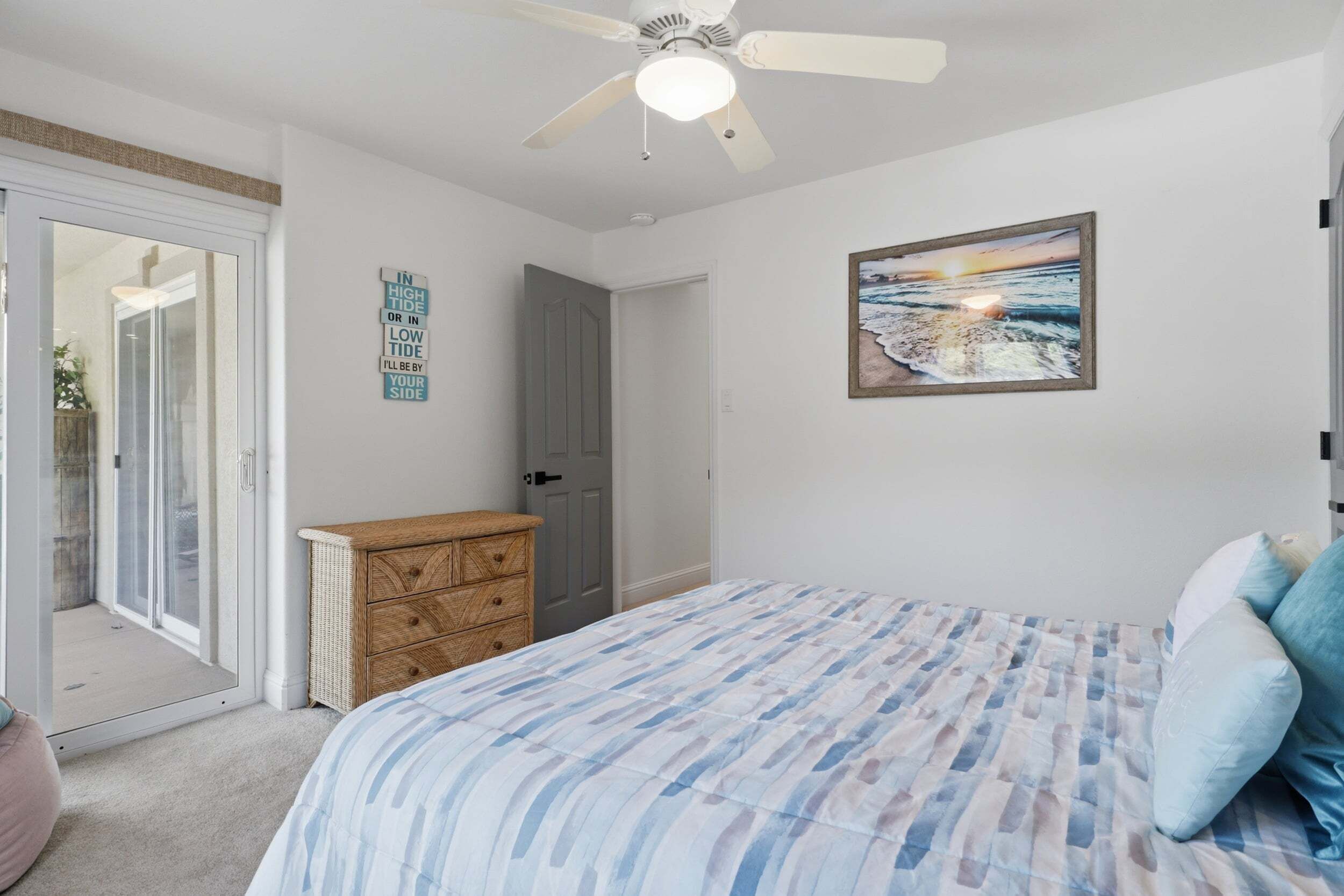 A bedroom with a bed, a dresser, a ceiling fan, and a door.