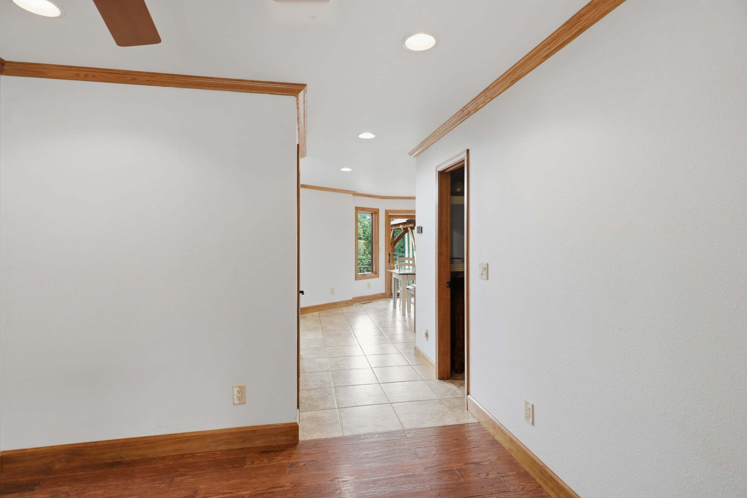 A hallway with wooden trim, white walls, and a tiled floor.