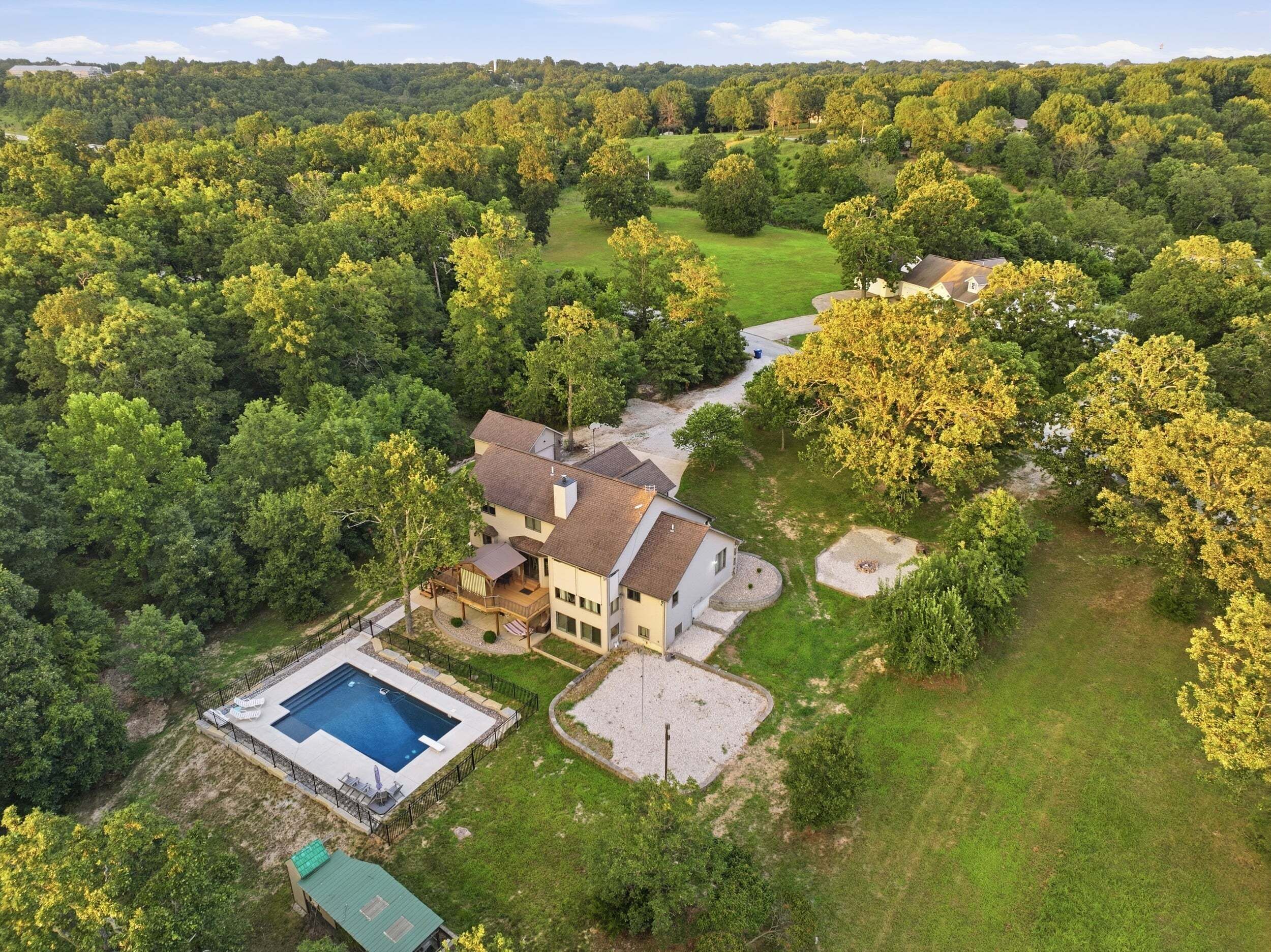 A two-story house with a swimming pool, surrounded by dense forest.