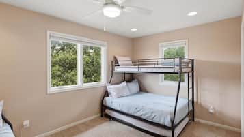 Habitación con literas, ventilador de techo, dos ventanas con vistas a árboles y piso alfombrado.
