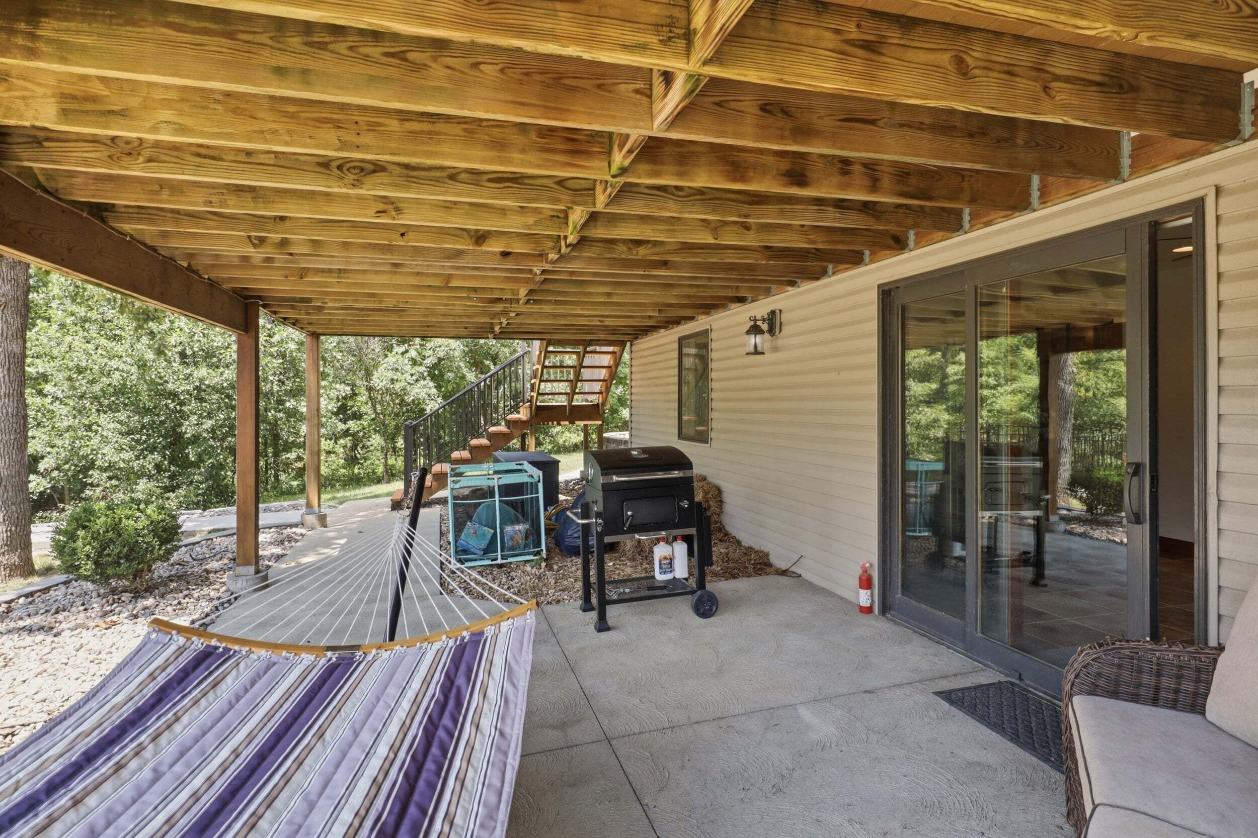 A covered patio area with a hammock, a grill, and a staircase leading to a glass door.