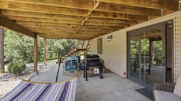 A covered patio area with a hammock, a grill, and a staircase leading to a glass door.