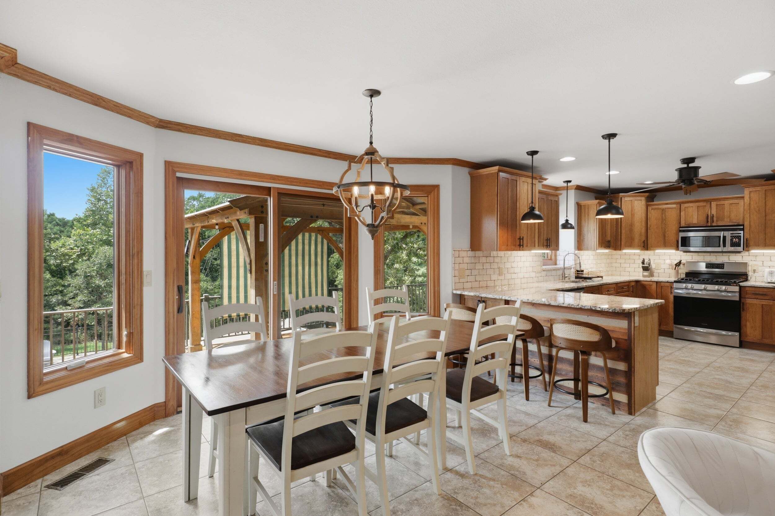A kitchen with wooden cabinets, a central island, and a dining area with chairs and a table.