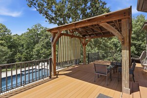 Una terraza de madera con pérgola, mobiliario exterior y piscina.