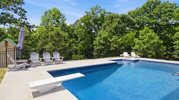 A swimming pool with lounge chairs and a deck area, surrounded by trees.