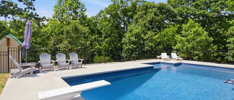 Una piscina con sillas de descanso y una terraza, rodeada de árboles.