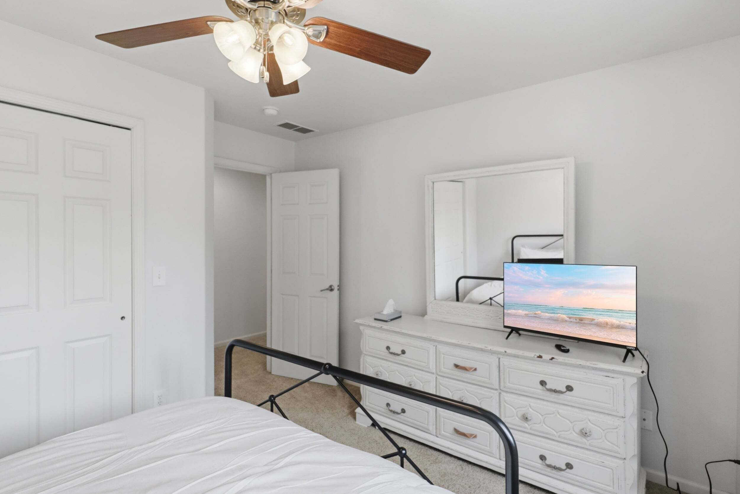 A bedroom with a bed, a dresser, a mirror, and a ceiling fan.