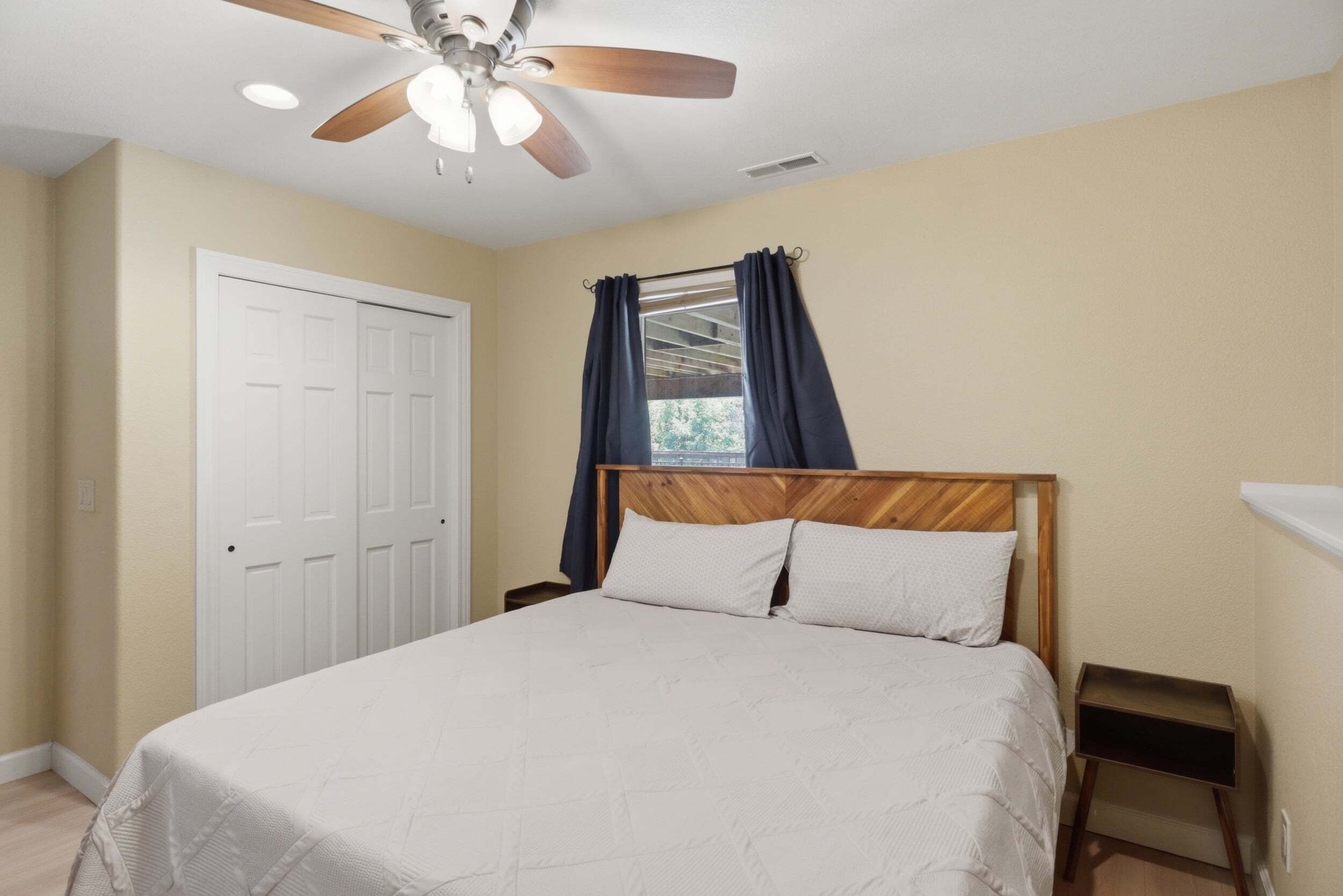 A bedroom with a bed, a ceiling fan, a window with curtains, and a door.
