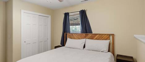 A bedroom with a bed, a ceiling fan, a window with curtains, and a door.