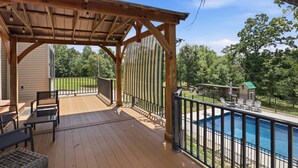 A wooden deck with outdoor furniture, a pool, and a view of a green landscape. - Private Heated Pool, Sleeps 18, Game Room & Outdoor Living (Camdenton)