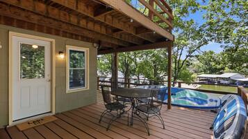 Una terraza de madera con un porche cubierto, una mesa con sillas y un jacuzzi.