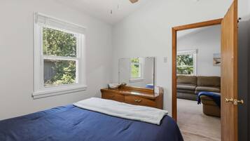 A bedroom with a bed, dresser, and a mirror. There is a window with a view of trees.