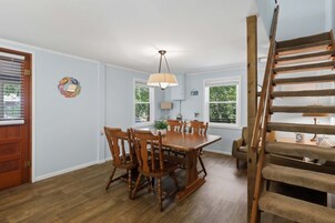 Comedor con mesa y sillas de madera, ventilador de techo y escalera con barandilla de madera.