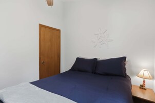 Un dormitorio con una cama, una mesita de noche con lámpara, una puerta de madera y un adorno en la pared.