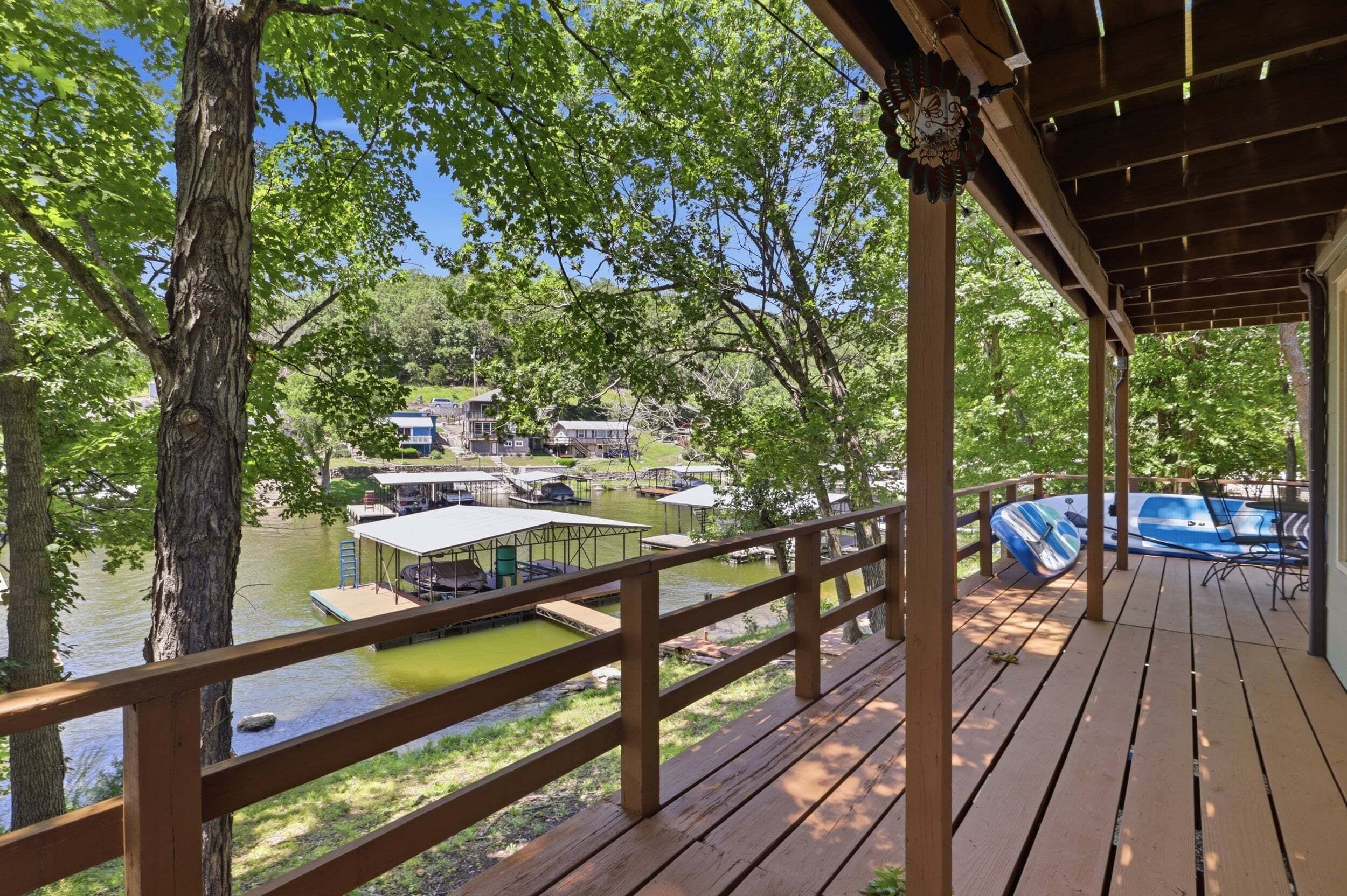 Una terraza de madera con vista a un lago, con barcos y casas al fondo.
