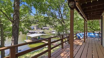 Una terraza de madera con vista a un lago, con barcos y casas al fondo.