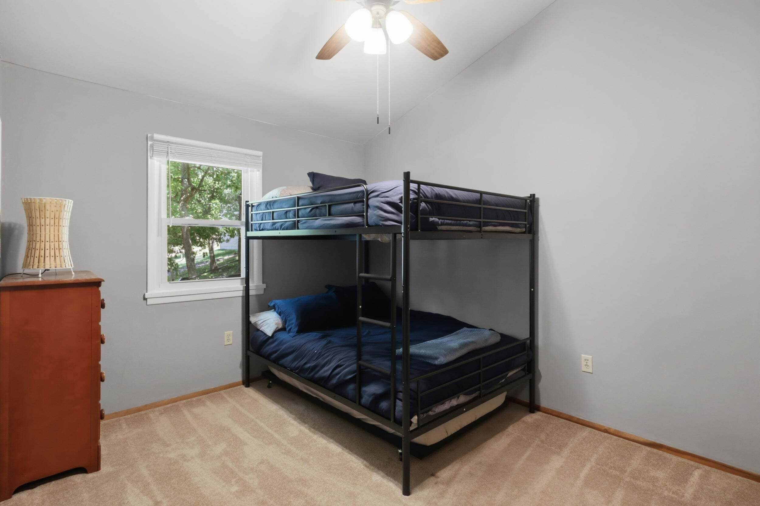 Habitación con literas, ventilador de techo, ventana con persianas y cómoda de madera.