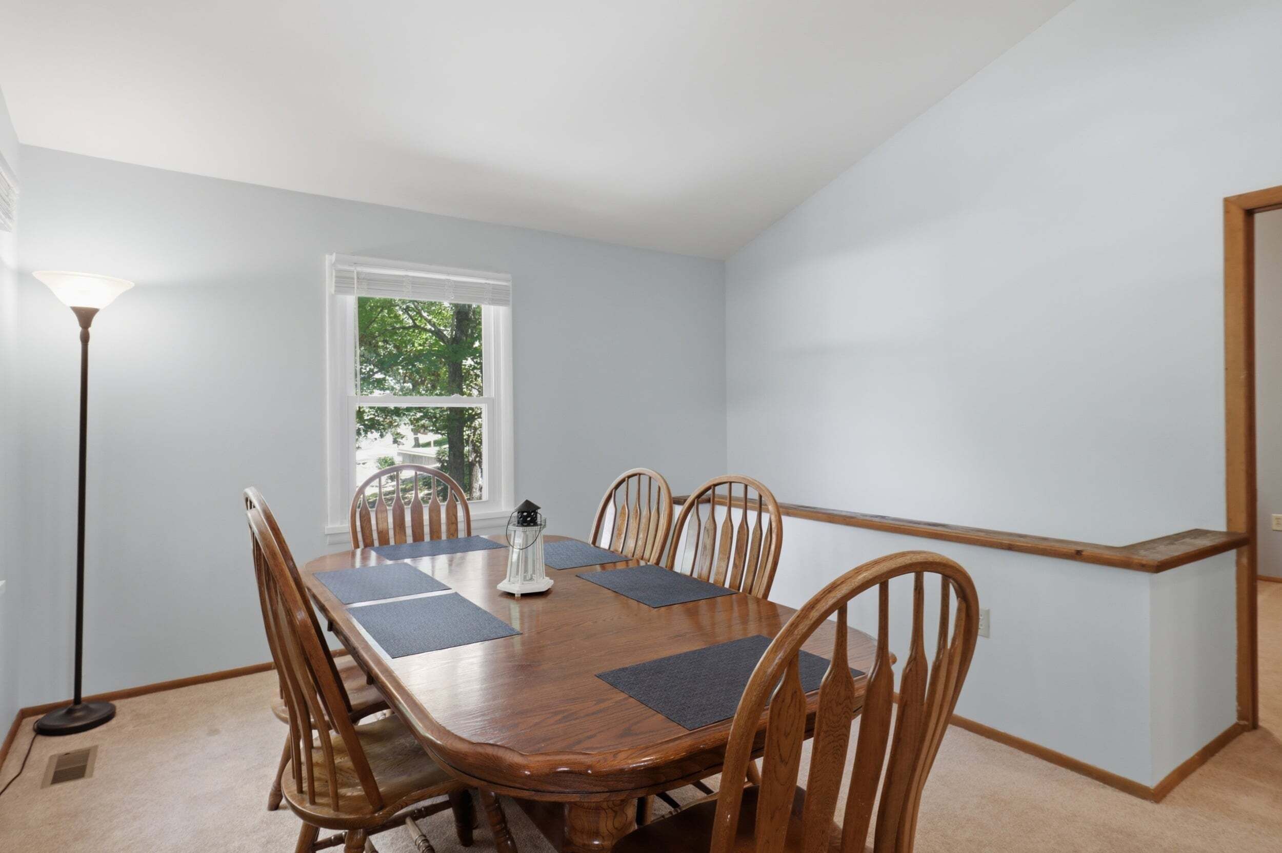 A dining room with a wooden table and chairs, a floor lamp, and a window with blinds.