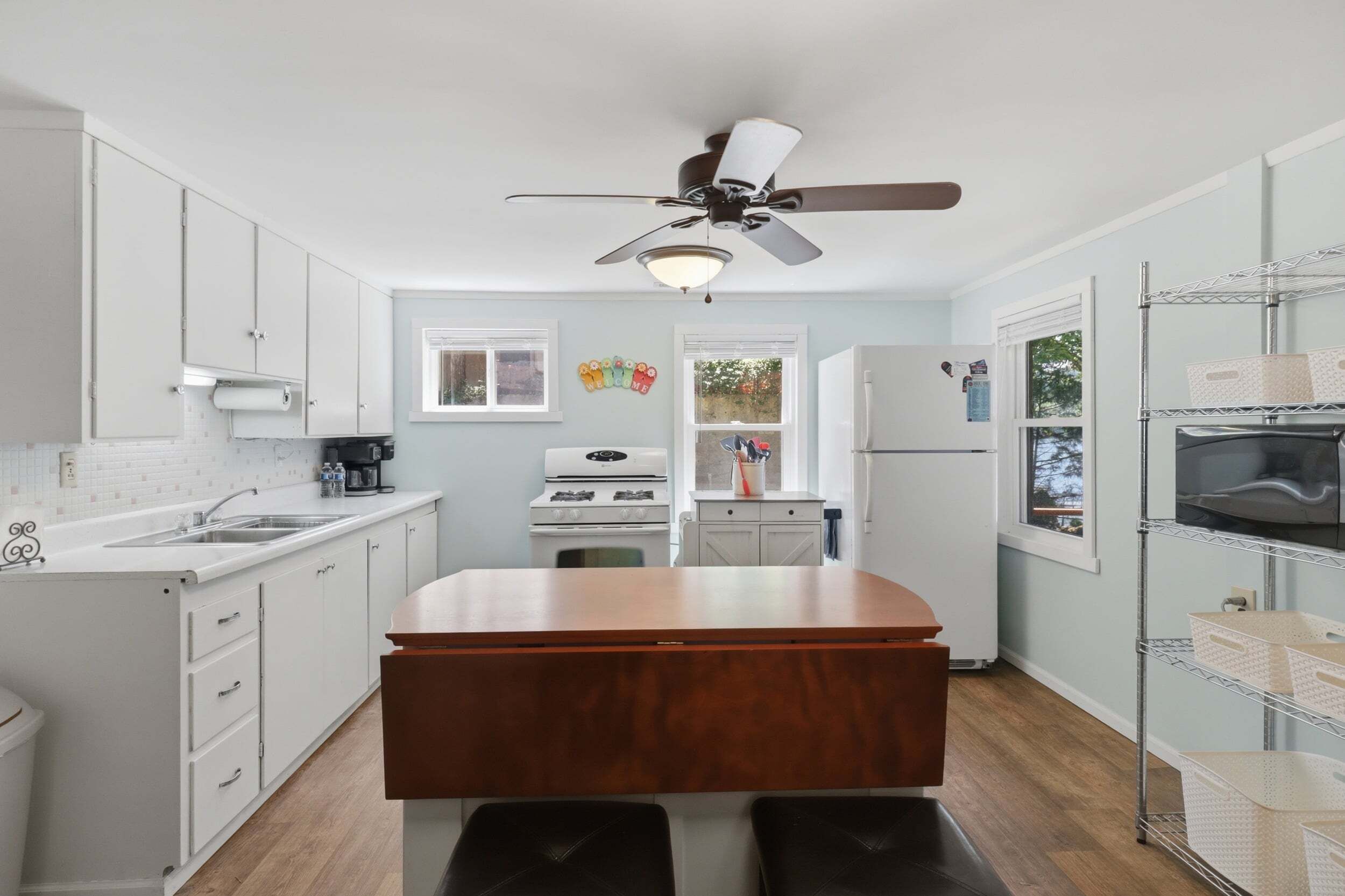 A compact kitchen with white cabinets, a central island, a ceiling fan, and a refrigerator.