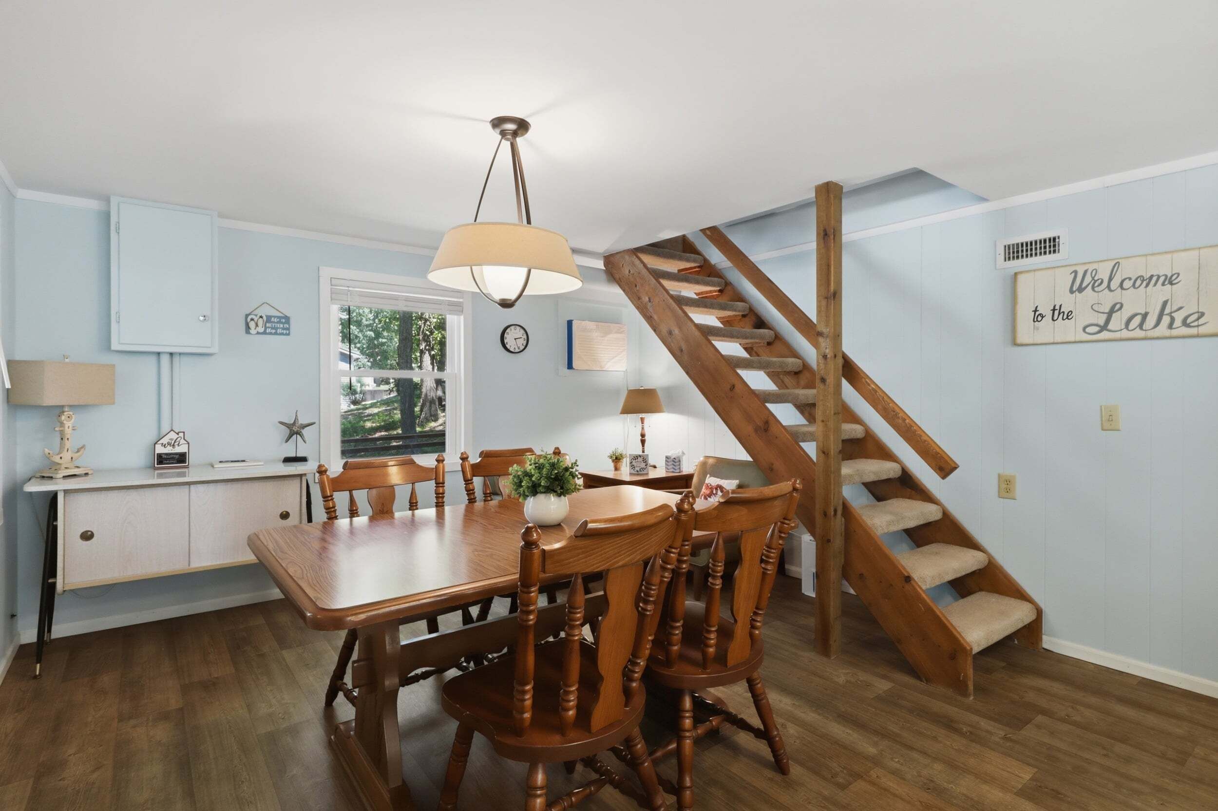A dining area with a wooden table and chairs, a chandelier, and a staircase leading to another level.