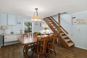 Een eetruimte met een houten tafel en stoelen, een kroonluchter en een trap naar een hoger niveau.