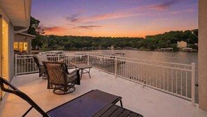 A balcony with outdoor furniture, a railing, and a view of a river at sunset. - Lake Fun Retreat w/ Sunroom, PWC & Boat Slip, Dock Slide & Views (Osage Beach)