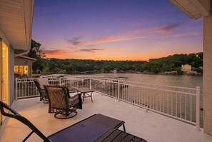 A balcony with outdoor furniture, a railing, and a view of a river at sunset. - Lake Fun Retreat w/ Sunroom, PWC & Boat Slip, Dock Slide & Views (Osage Beach)