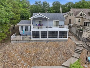 A two-story house with a covered porch and a stone retaining wall. - Lake Fun Retreat w/ Sunroom, PWC & Boat Slip, Dock Slide & Views (Osage Beach)