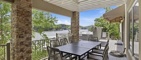 A covered outdoor deck with a table and chairs, stone pillars, and a view of a body of water.