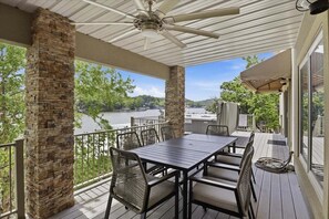 A covered outdoor deck with a table and chairs, stone pillars, and a view of a body of water. - Perfect Lake Life at Bulldog Lake House! Huge Dock, Dock Bar, Decks & Fun at 2mm! (Lake Ozark)