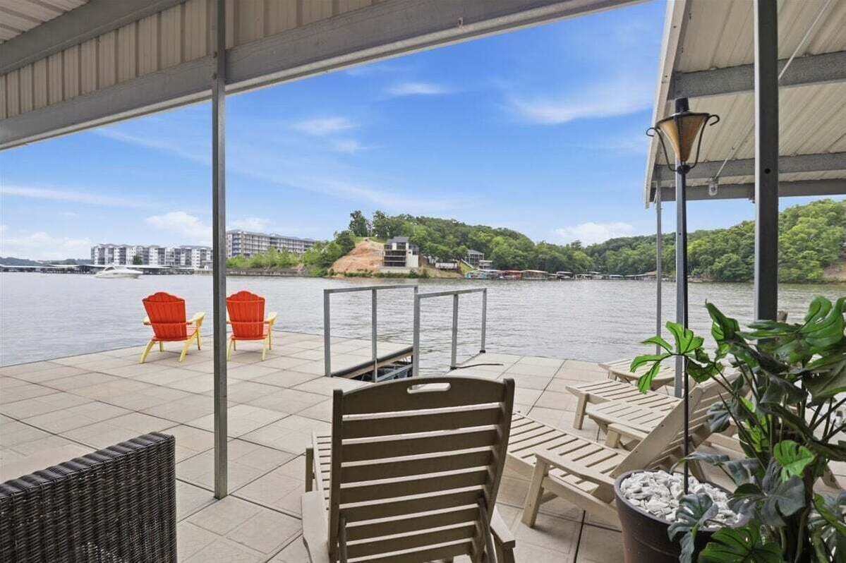 Un espace extérieur abrité, doté de chaises et de tables, offrant une vue sur une étendue d’eau et sur des bâtiments situés au loin.