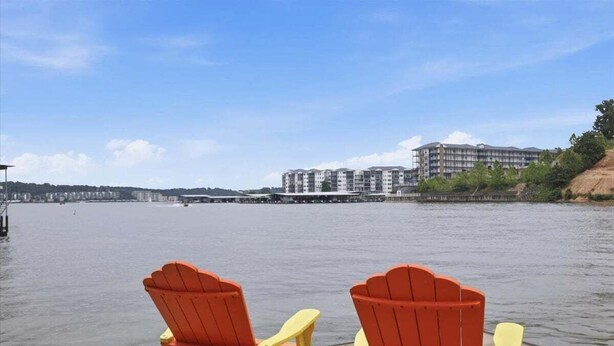 Two red Adirondack chairs facing a body of water with a building in the background. - Perfect Lake Life at Bulldog Lake House! Huge Dock, Dock Bar, Decks & Fun at 2mm! (Lake Ozark)