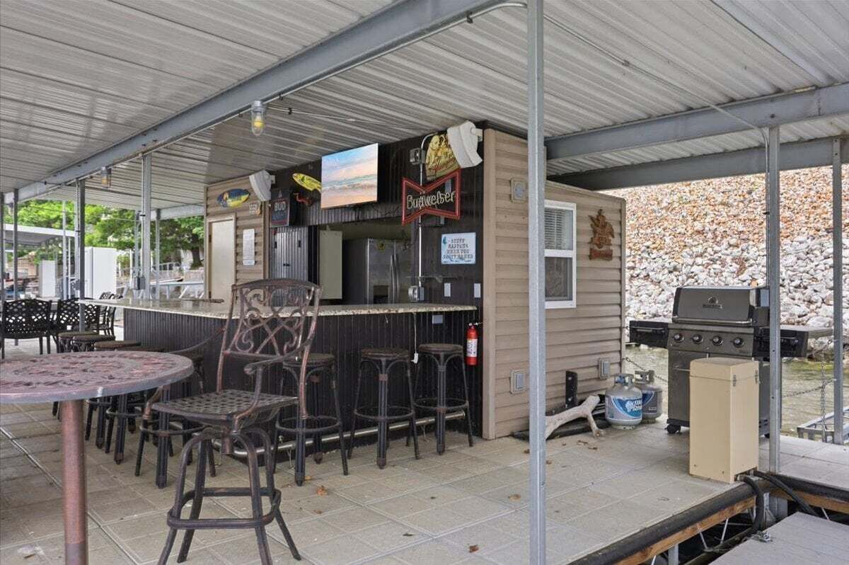 Un espace bar extérieur comprenant un barbecue, des tabourets de bar et un coin salon abrité.
