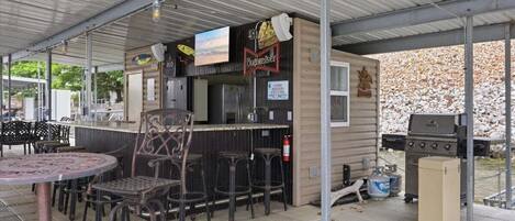 Een buitengebied met een bar, een barbecue, barkrukken en een overdekt zitgedeelte.