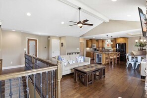 A spacious living area with a high ceiling fan, wooden flooring, a sofa, and a dining area with chairs. - Perfect Lake Life at Bulldog Lake House! Huge Dock, Dock Bar, Decks & Fun at 2mm! (Lake Ozark)