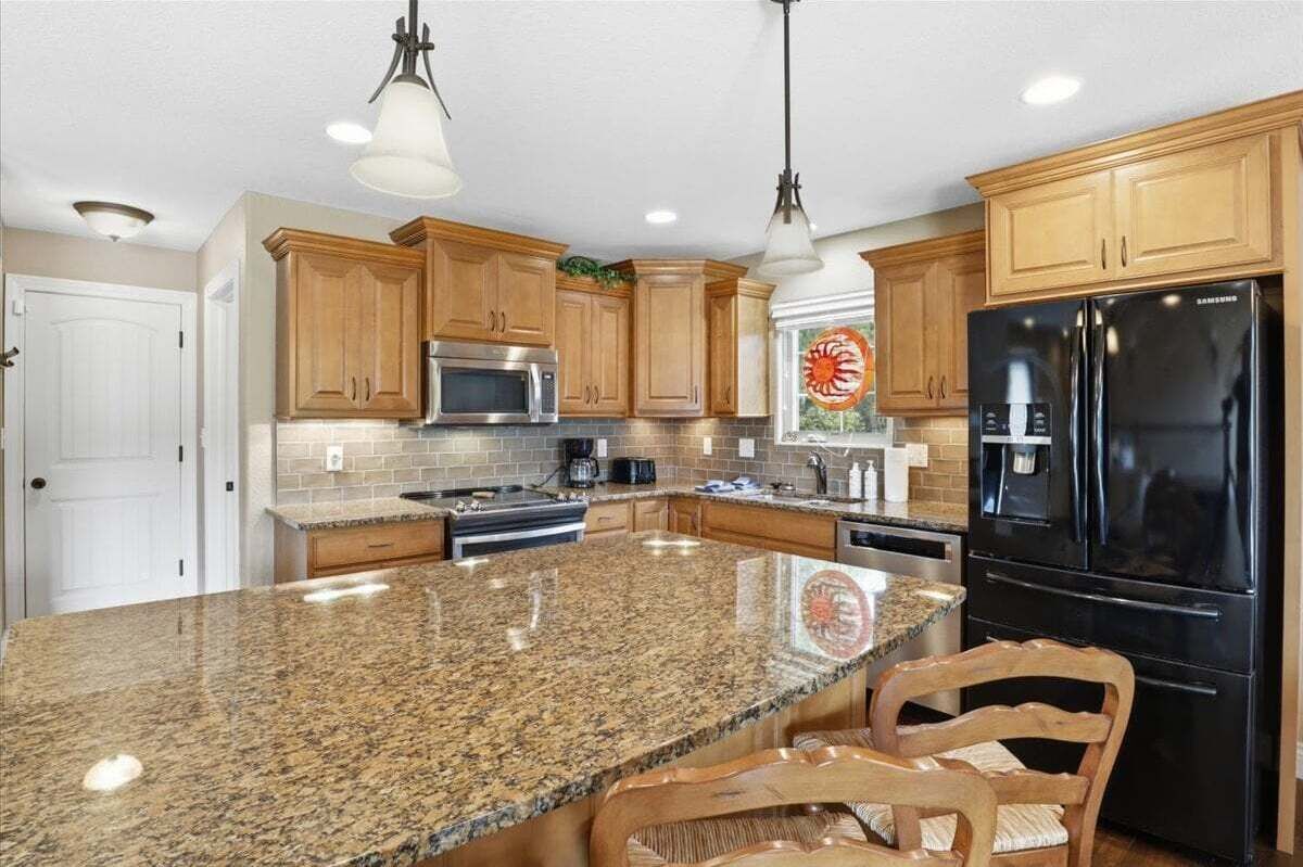 Una cocina con encimeras de granito, armarios de madera, electrodomésticos de acero inoxidable e iluminación colgante.