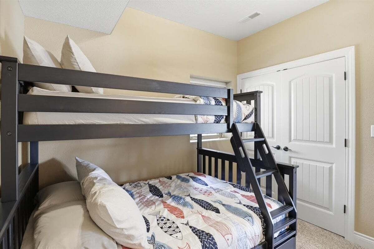A bunk bed with a patterned bedspread and pillows, a white door, and a staircase.