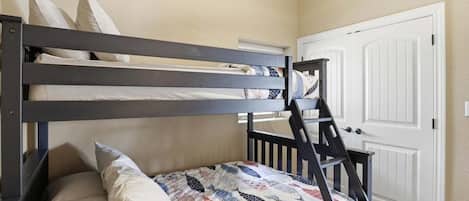 A bunk bed with a patterned bedspread and pillows, a white door, and a staircase.