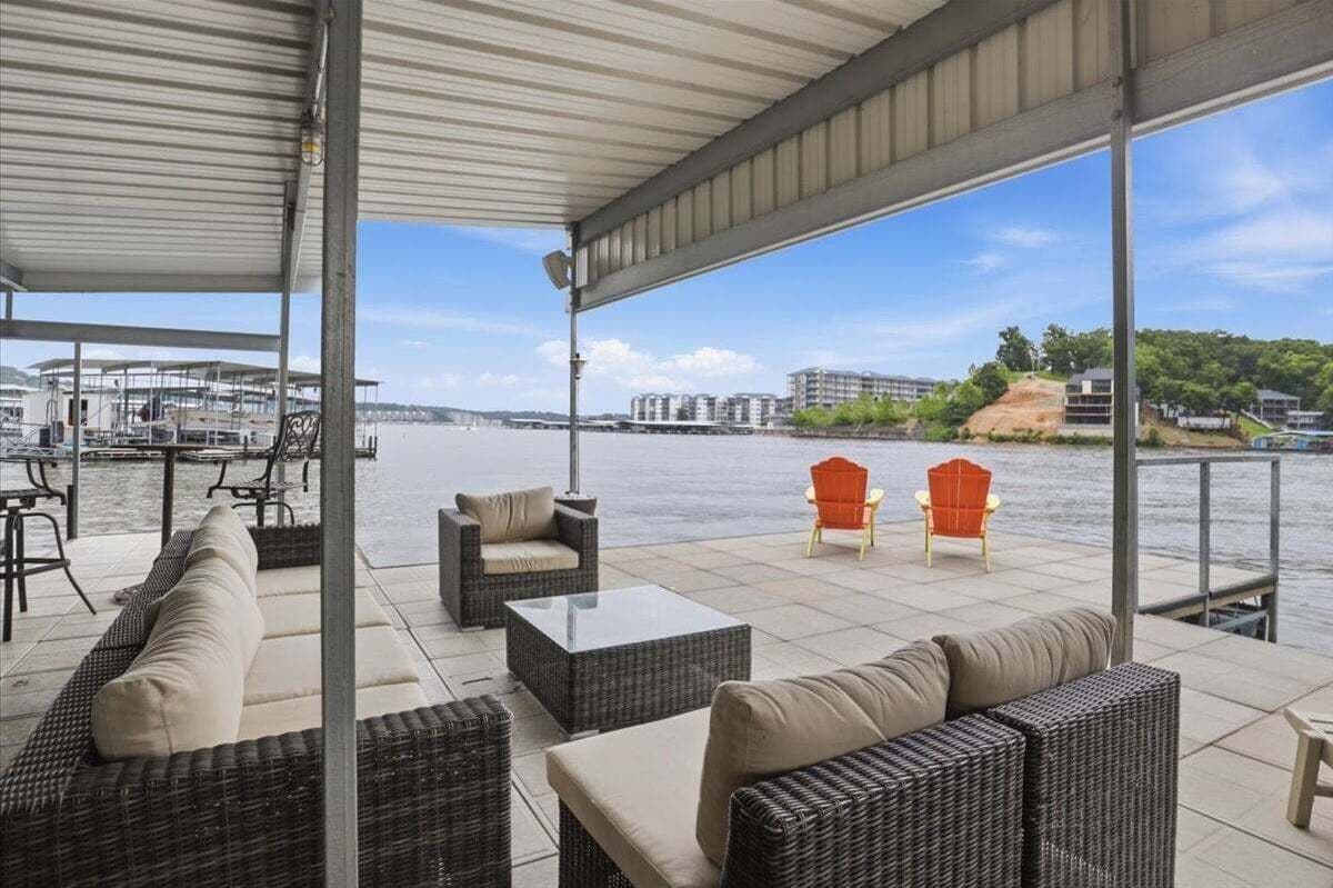 A covered outdoor seating area with wicker furniture and a view of a river and buildings.